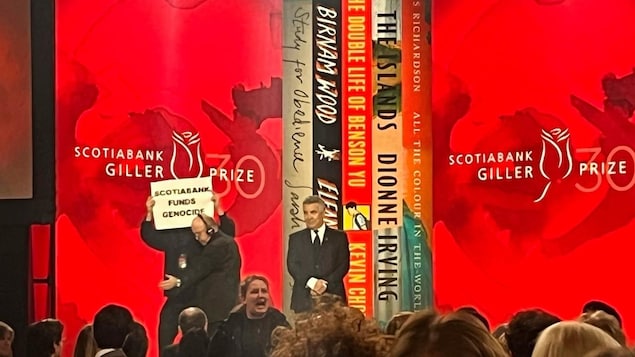 A protester on stage holds a sign saying "Scotiabank funds genocide" at November's Scotiabank Giller Prize ceremony.