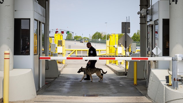 Un agent américain tient un chien renifleur avec sa laisse devant une barrière fermée d'un poste frontalier le 23 mai 2023.