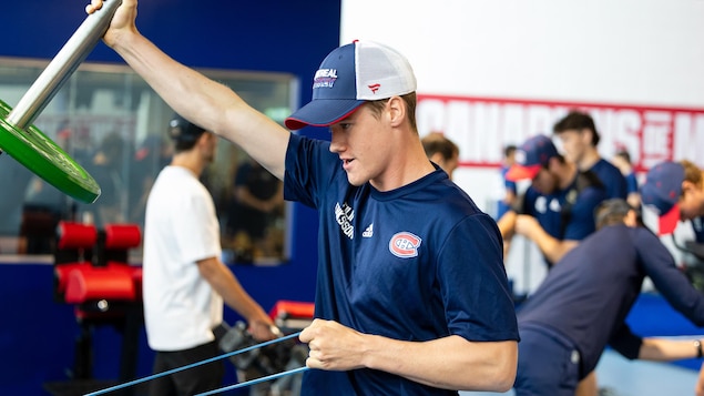 Un joueur de hockey à l'allure très jeune utilise de l'équipement en gymnase au milieu de ses coéquipiers.