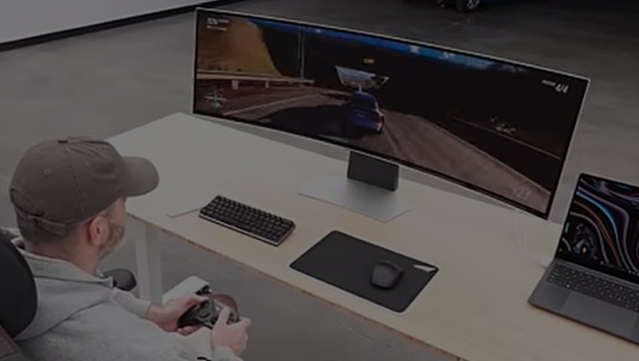 A man sits at a desk in front of the OLED G9 playing a racing game with a controller.