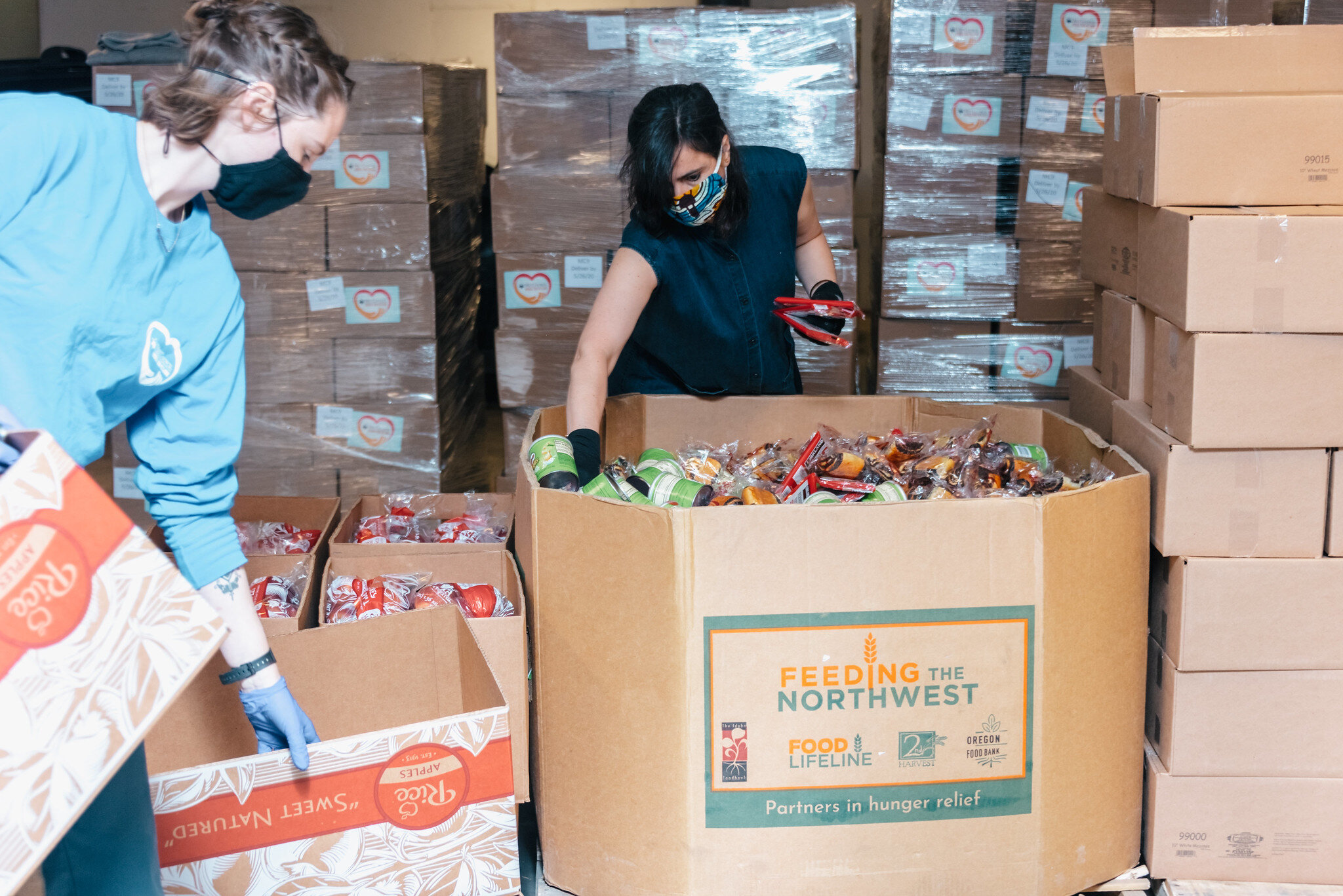 Inside Met Council's Greenpoint fulfillment center, two volunteers grab food to package while wearing face masks.