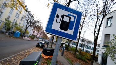 Ein Schild und eine Ladesäule stehen an einer Straße.