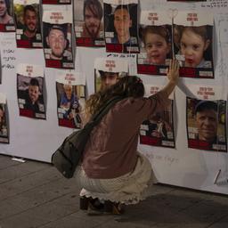 Eine Frau kniet vor einer Wand mit Fotos von Israelis, die in Gaza vermisst und gefangen gehalten werden.