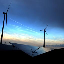 Windräder vor blauem Himmel, am Boden sieht man eine Solaranlage.