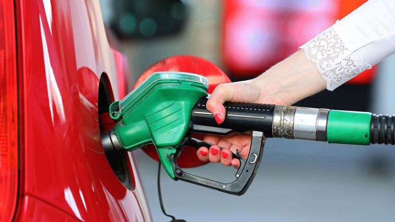 Eine Frau hält an einer Tankstelle an einer Zapfsäule eine Zapfpistole in der Hand und betankt ein Auto.