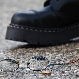 Zerbrochene Brille neben Springerstiefeln liegt auf dem Boden