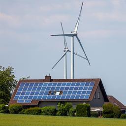 Einfamilienhäuser mit Photovoltaikanlagen auf den Dächern und im Hintergrund ein Windpark.