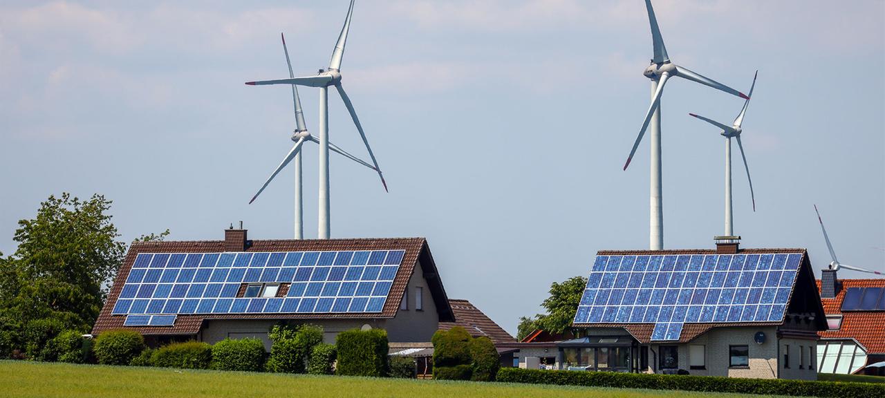 Einfamilienhäuser mit Photovoltaikanlagen auf den Dächern und im Hintergrund ein Windpark.