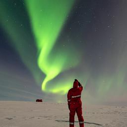 Ein Mann beobachtet Polarlichter über einer Schneelandschaft in der Antarktis.