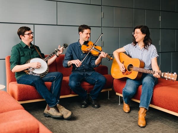 three musicians sitting with banjo, violin, and guitar