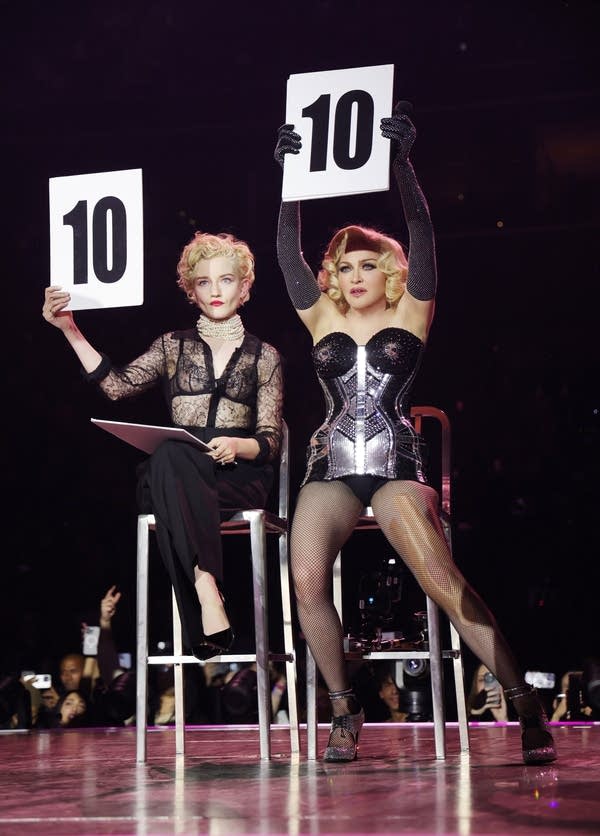 Two people hold up number cards as if judging a competition