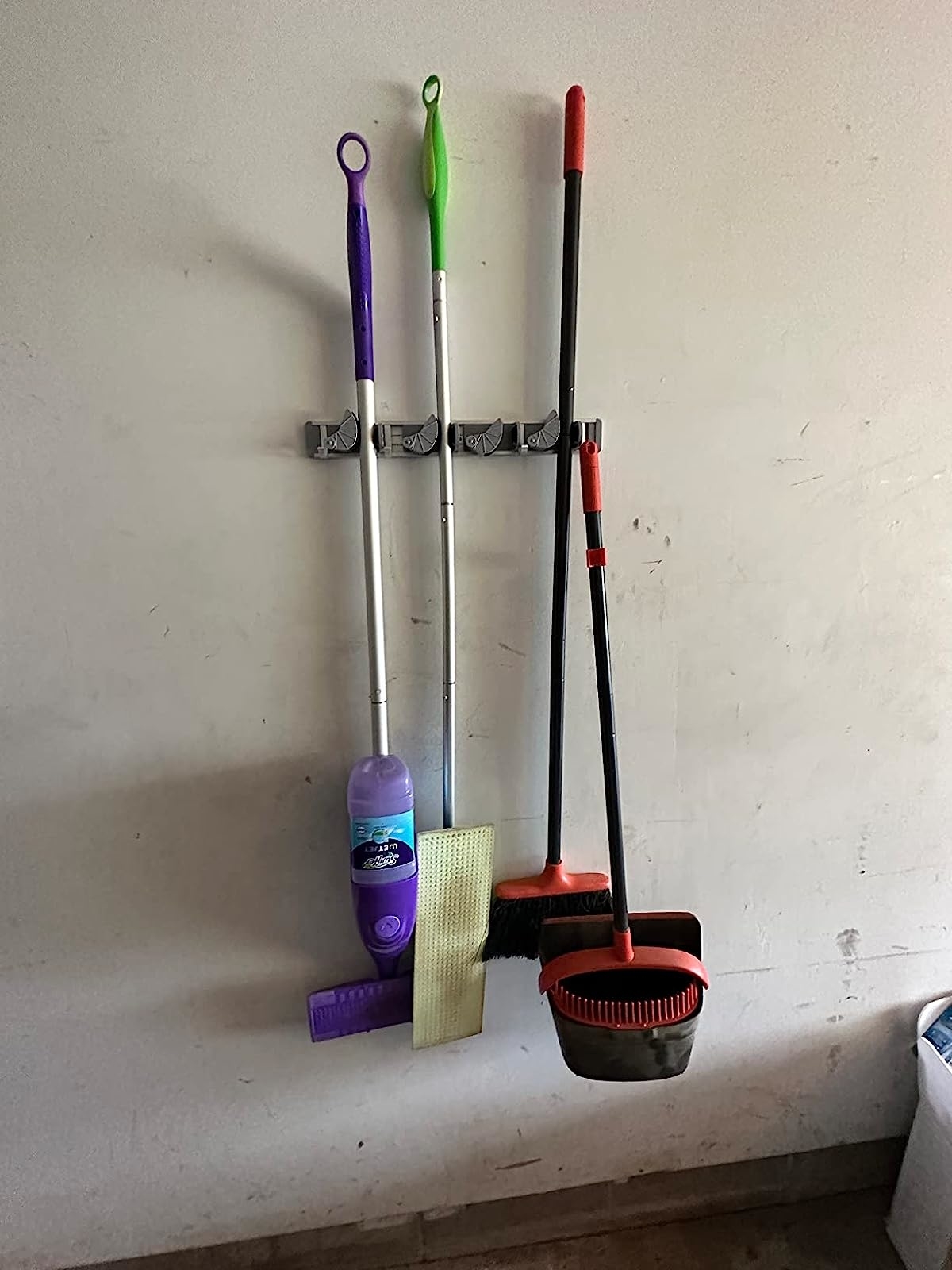 Reviewer&#x27;s swiffer, brooms, and mop hanging in holder on wall