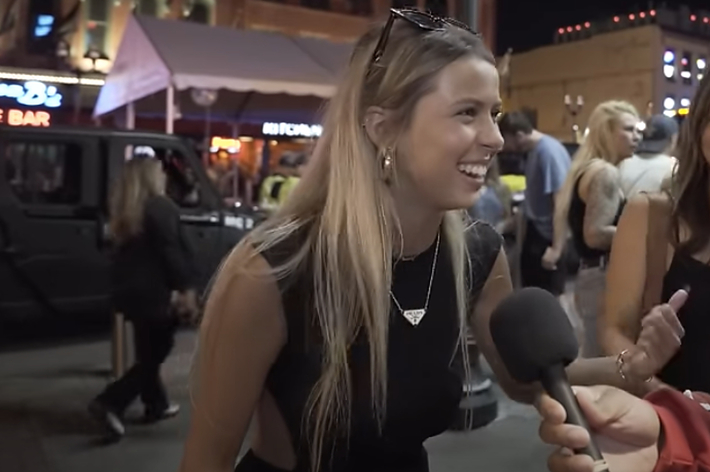 Two women laughing and interacting with a person holding a microphone on a lively street at night