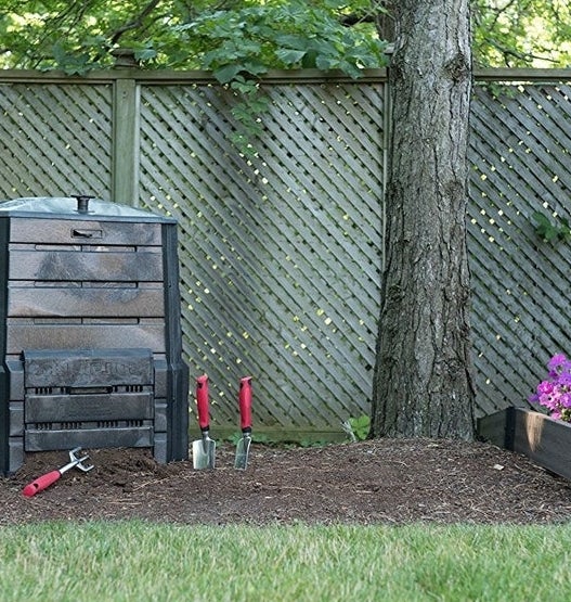 Backyard setup with a compost bin, a tree, planters of flowers, and garden tools