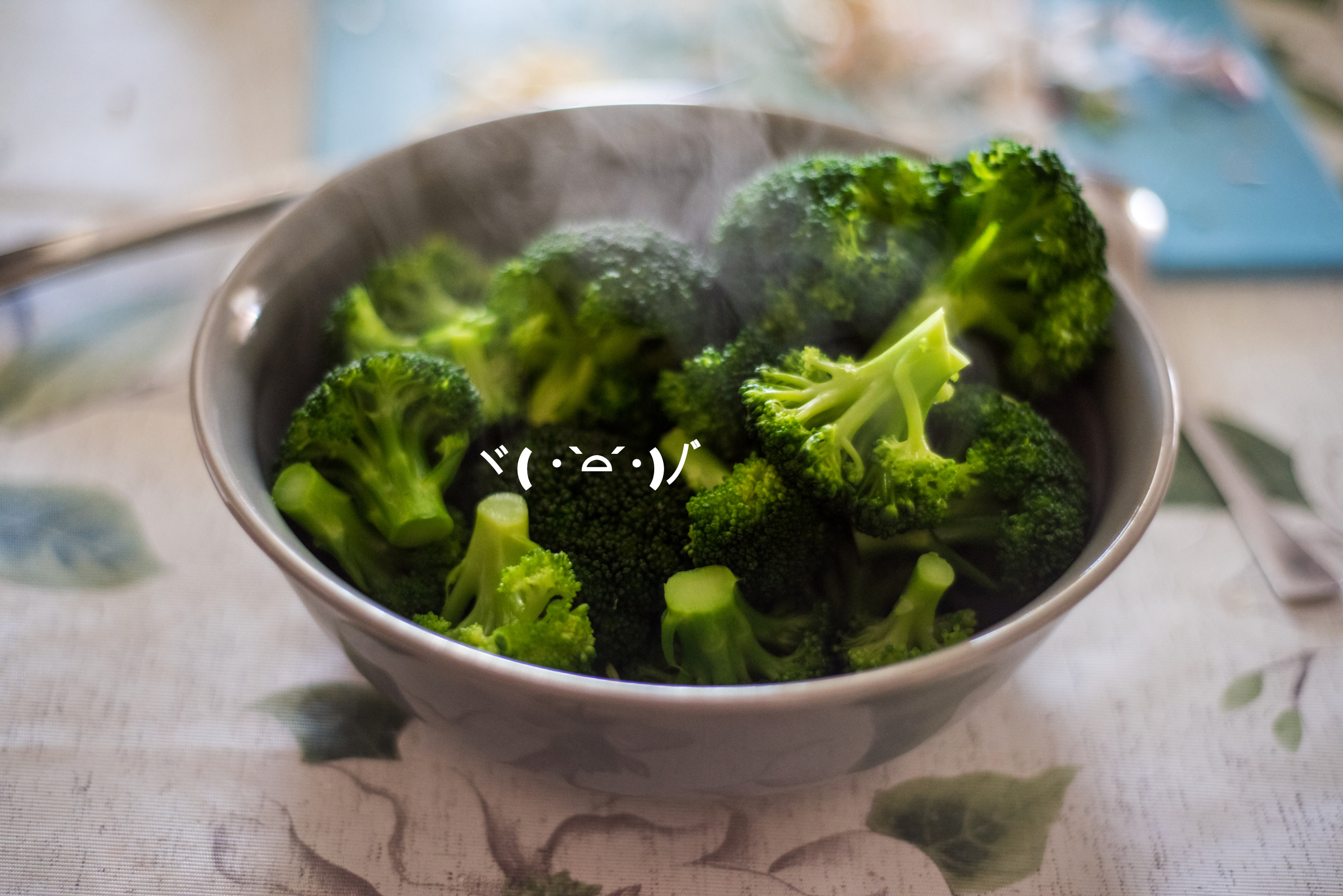 A steaming bowl of broccoli with an emoticon (╯°□°）╯