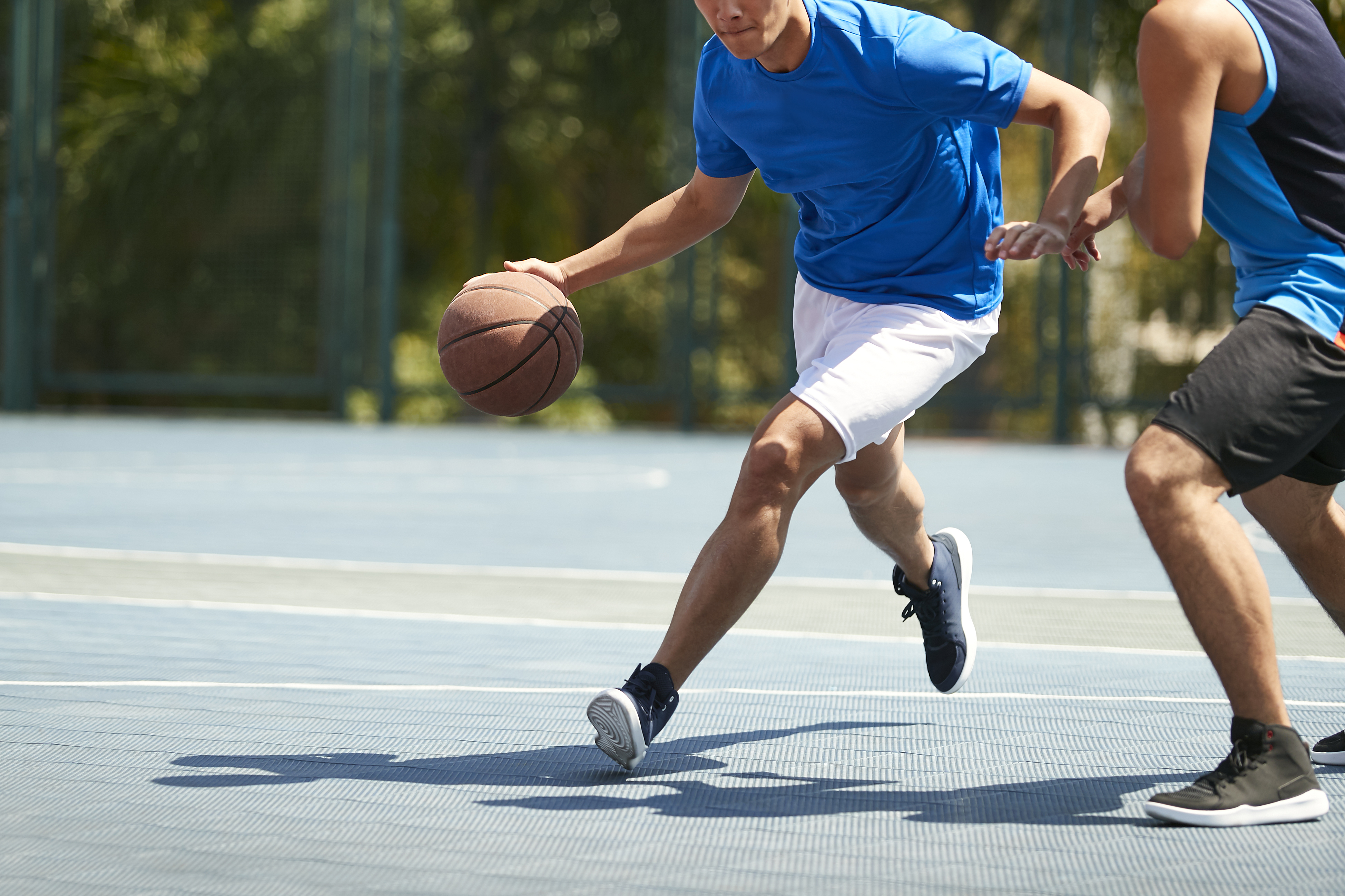 Two people playing basketball outdoors. One dribbles the ball in mid-action, while the other defends. No celebrity or red carpet context present