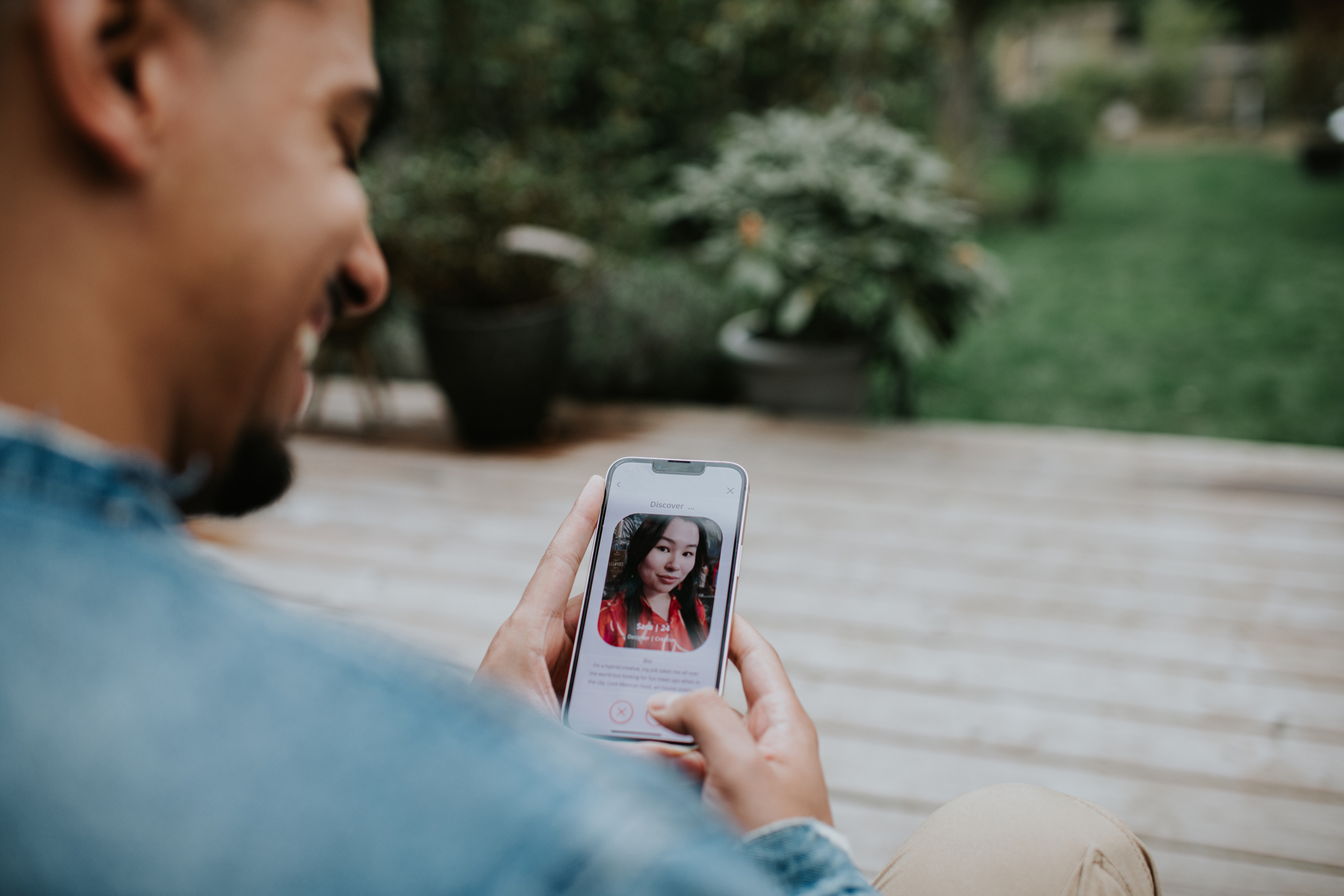 Person using a dating app on a smartphone outdoors, looking at a profile picture of a woman with long hair