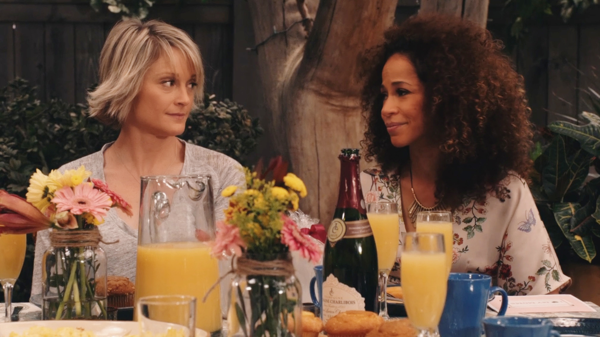 Teri Polo and Sherri Saum sit at a table with mimosa glasses in &quot;The Fosters.&quot;