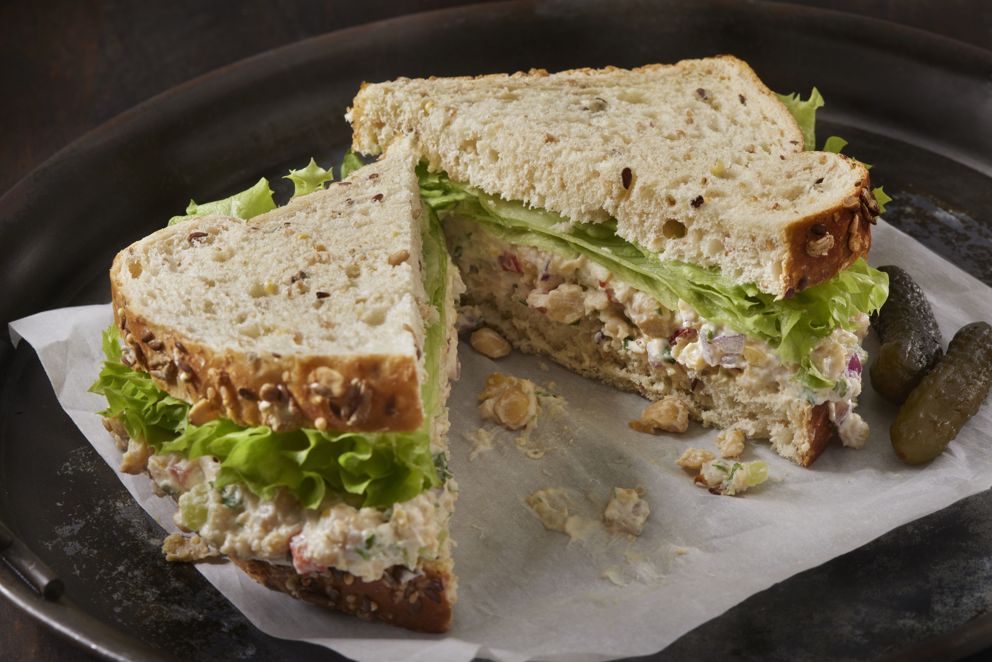 Chicken salad sandwich with lettuce on whole grain bread, served on a tray with pickles