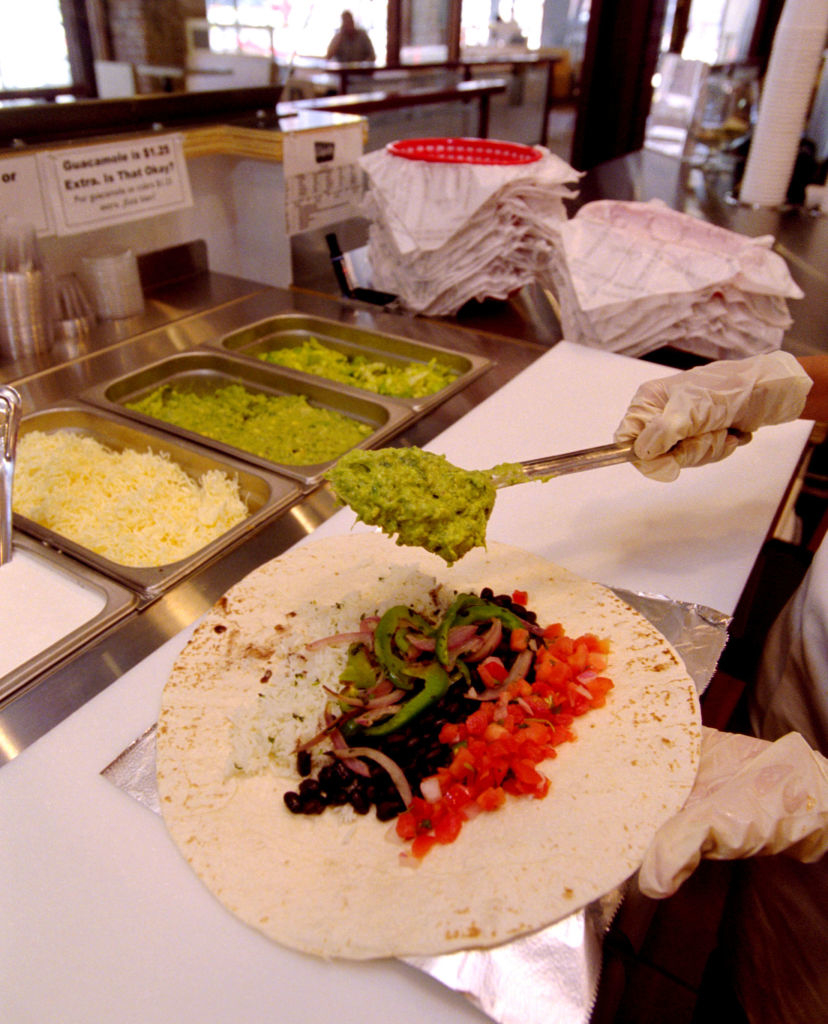 Burrito being prepared with ingredients like guacamole, beans, rice, and vegetables in a restaurant setting