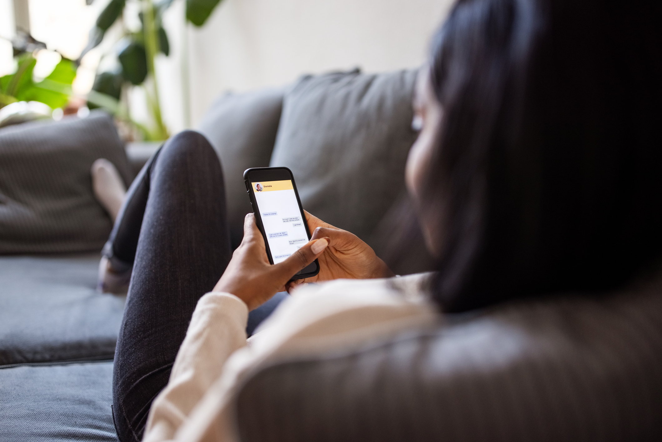 Person lounging on a couch, using a smartphone. The setting suggests casual, relaxed engagement with technology, possibly texting or browsing