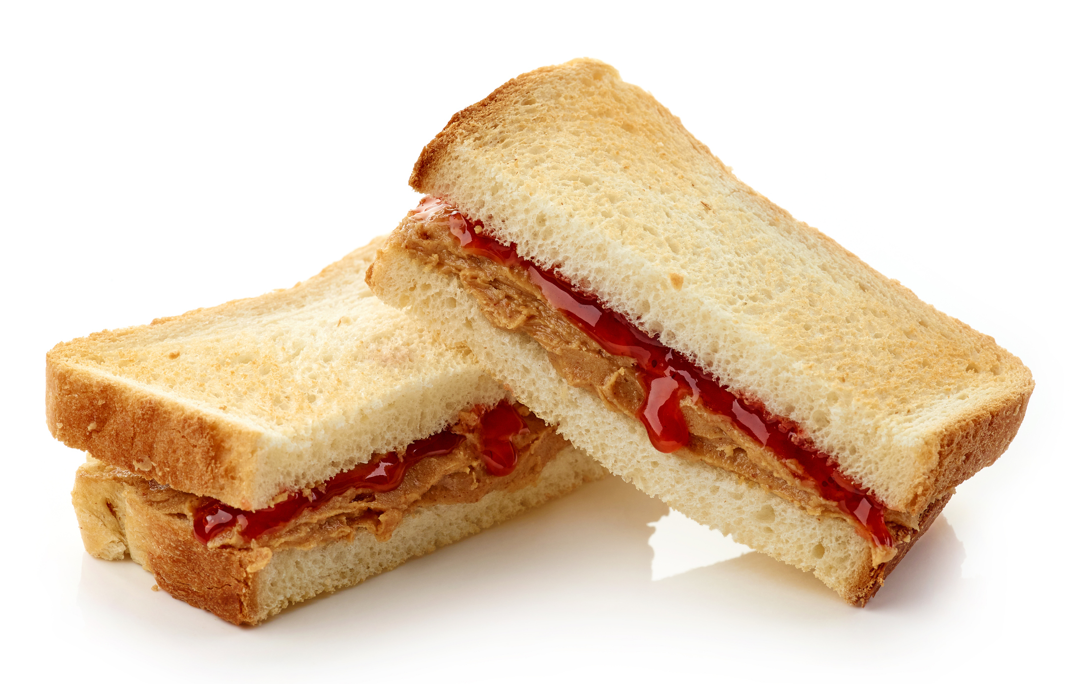 A peanut butter and jelly sandwich is cut in half and stacked on a white background