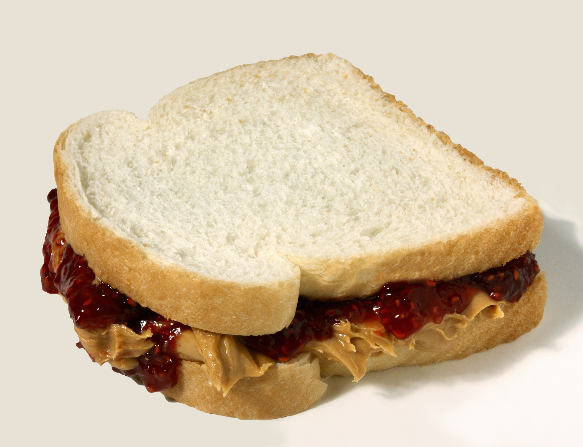 Peanut butter and jelly sandwich with white bread, neatly sliced, showing creamy peanut butter and berry jelly filling