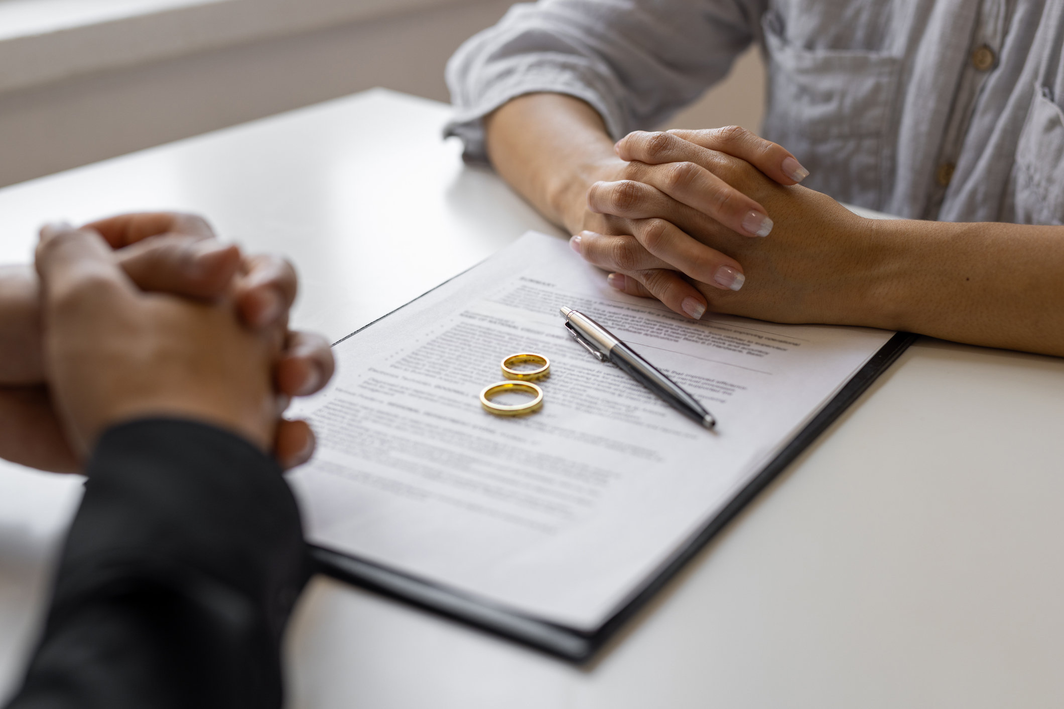 Two people sit across a table from each other, with a set of wedding rings and a pen placed on a document between them