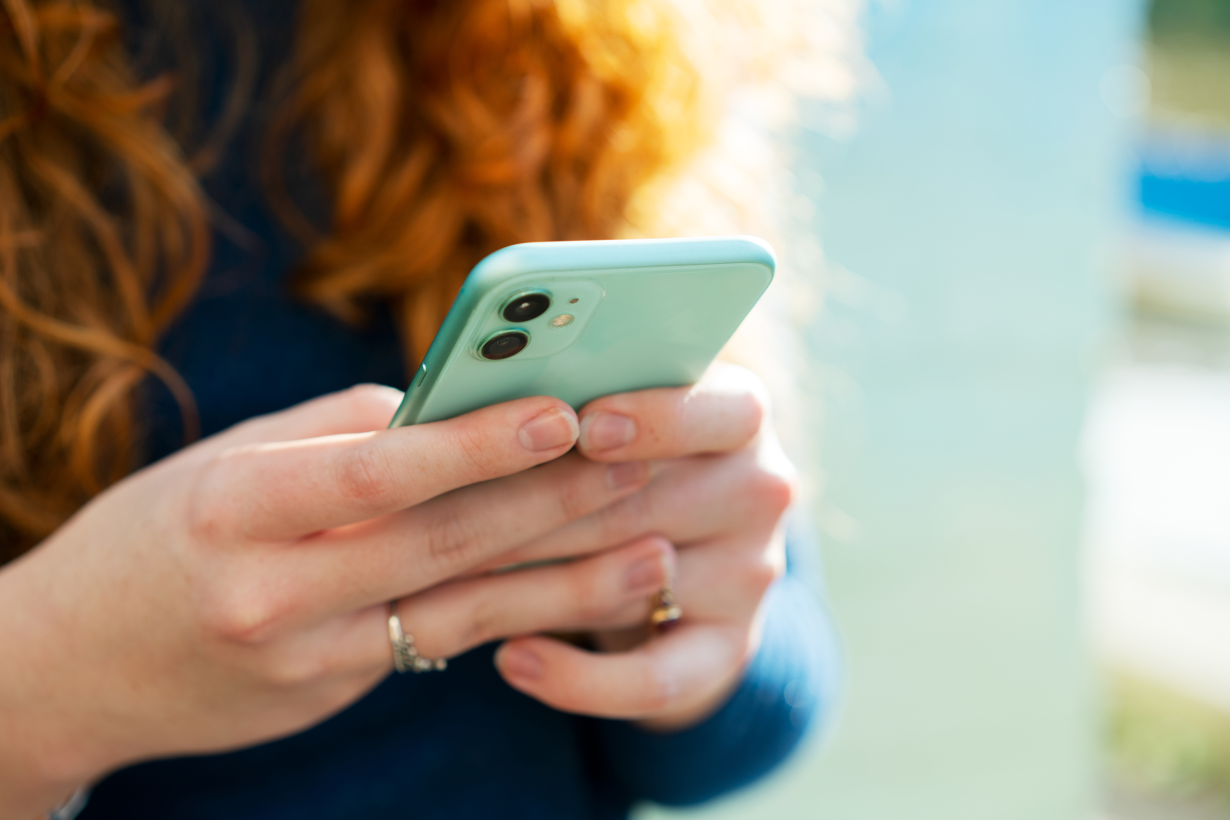 Person with long hair holding a smartphone, engaged in texting or browsing, suggesting a focus on digital communication in relationships