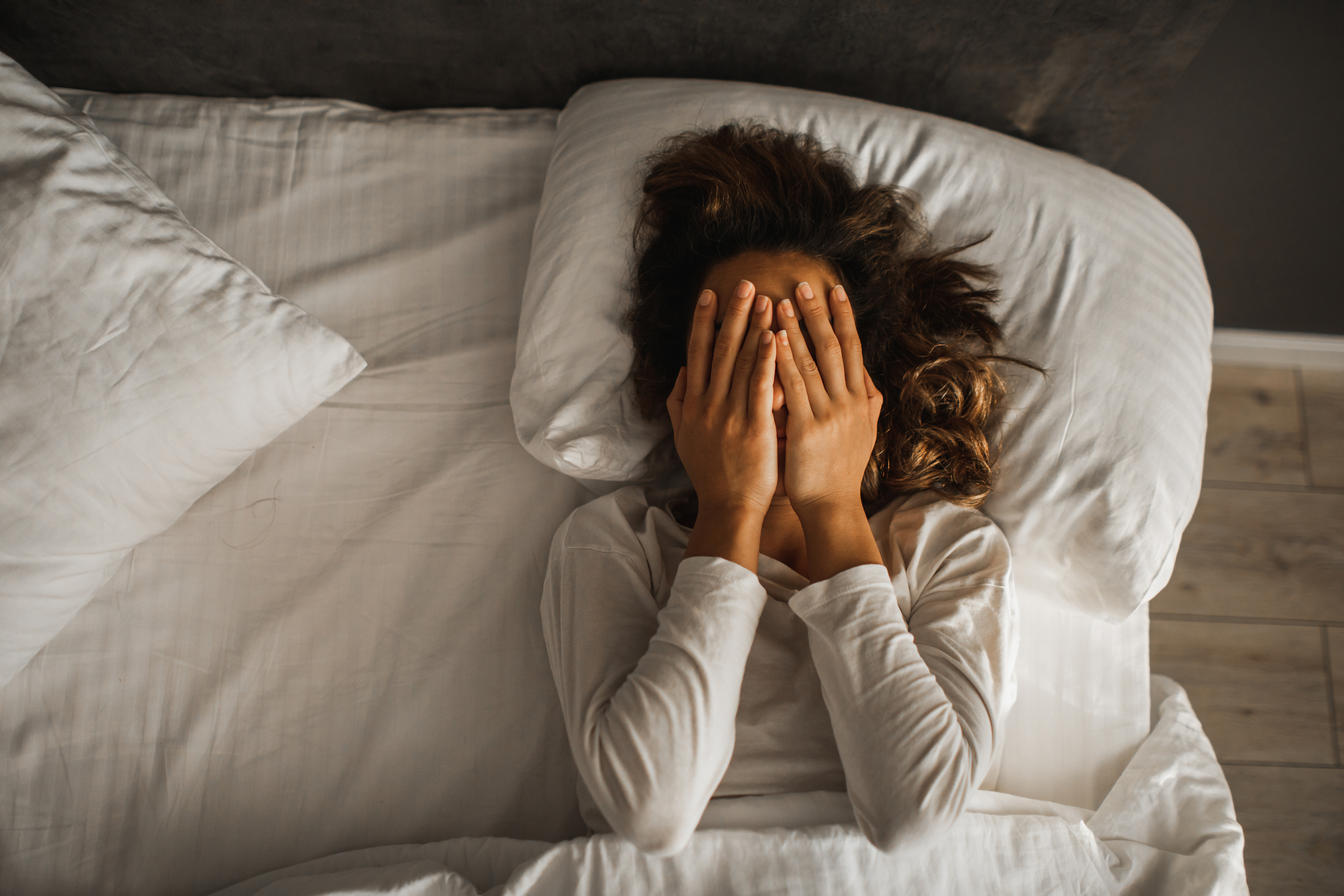 Person lying in bed covering their face with hands, expressing a sense of emotional weariness or contemplation