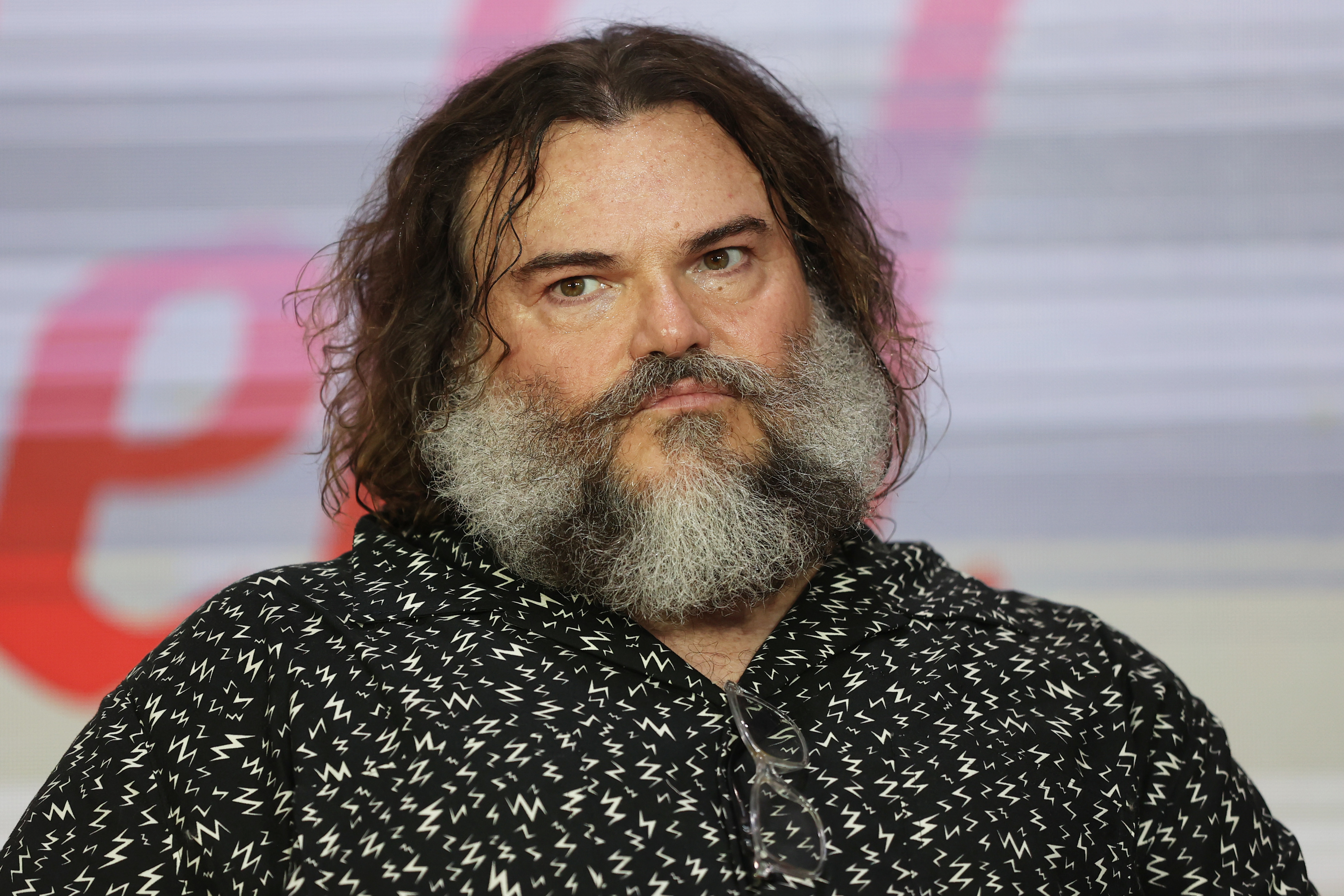 Man with a thick white beard in a patterned shirt at an event, looking thoughtful