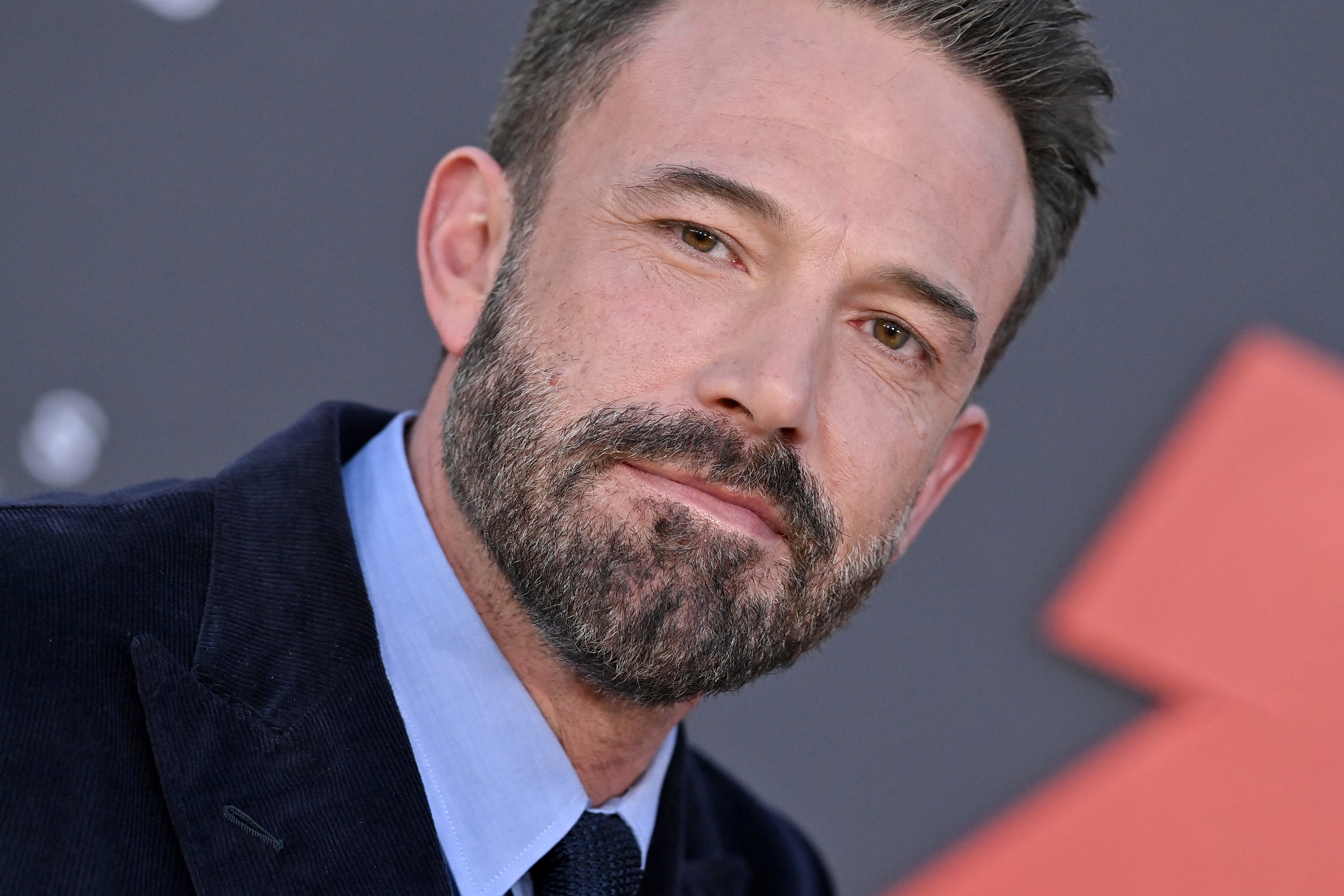 A man in formal attire with a beard looks towards the camera at a public event