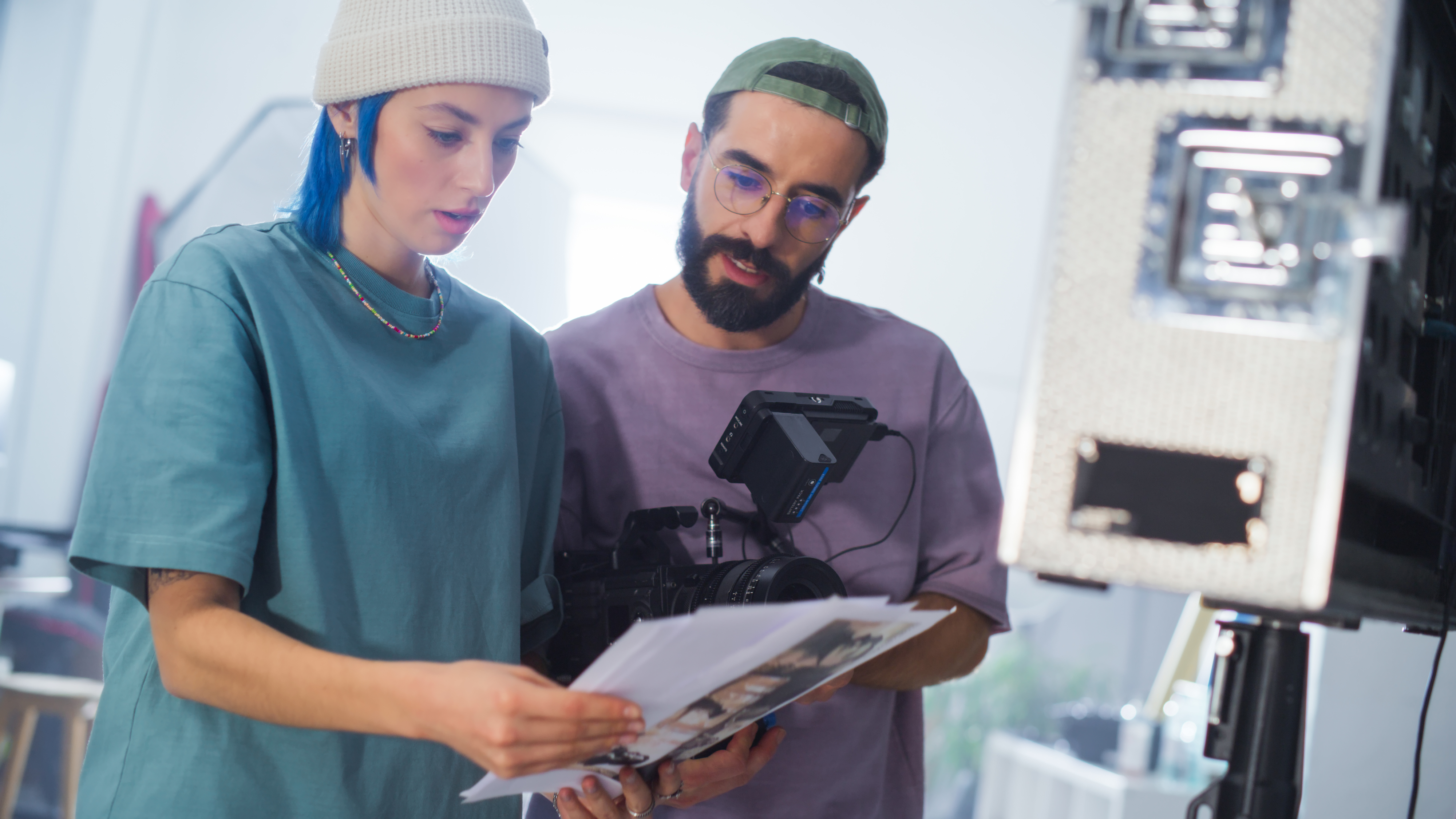 Two people in casual clothing review paper notes on a film set with a camera nearby