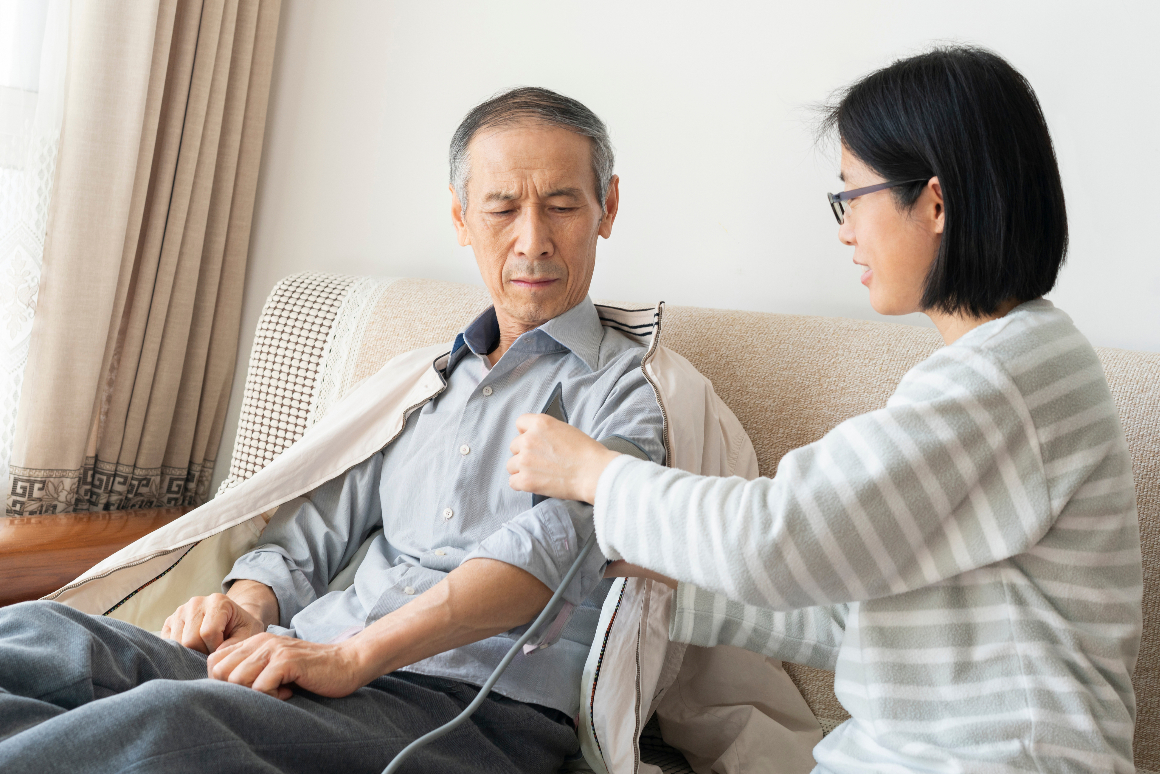 A woman checks a man&#x27;s blood pressure on a couch at home, showing a caring interaction in a domestic setting