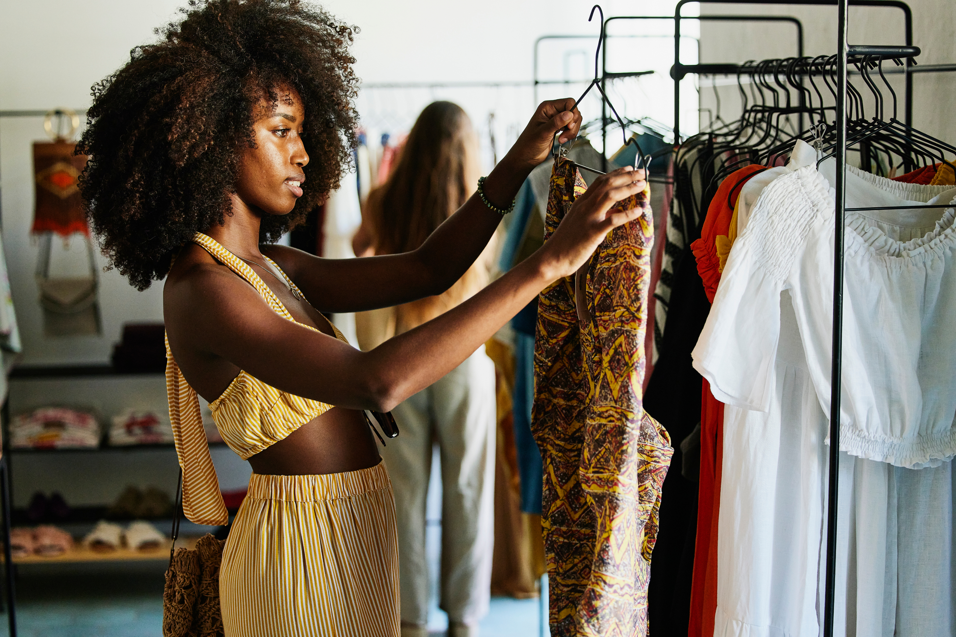 A person in a stylish striped outfit examines a patterned dress on a rack in a clothing store