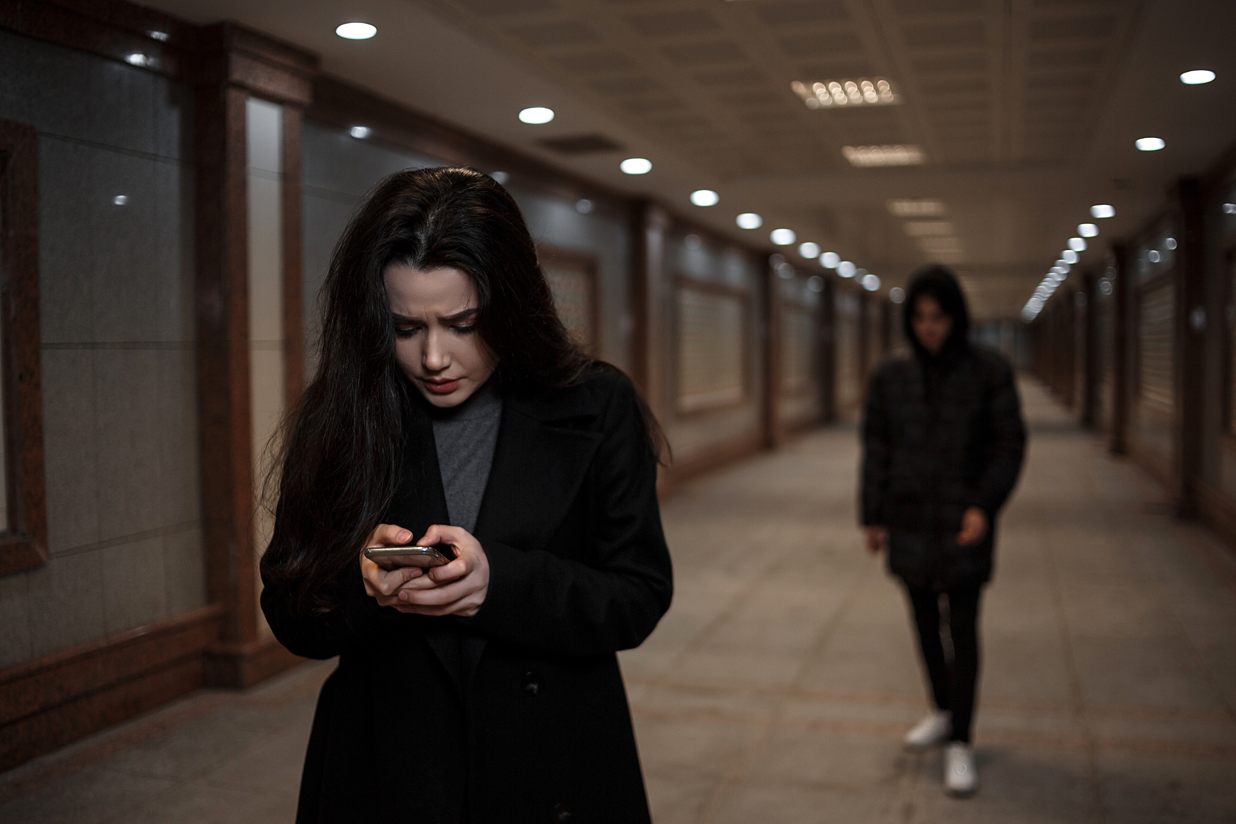 Woman looking at phone in subway tunnel while another person walks behind her. The setting appears tense and dramatic