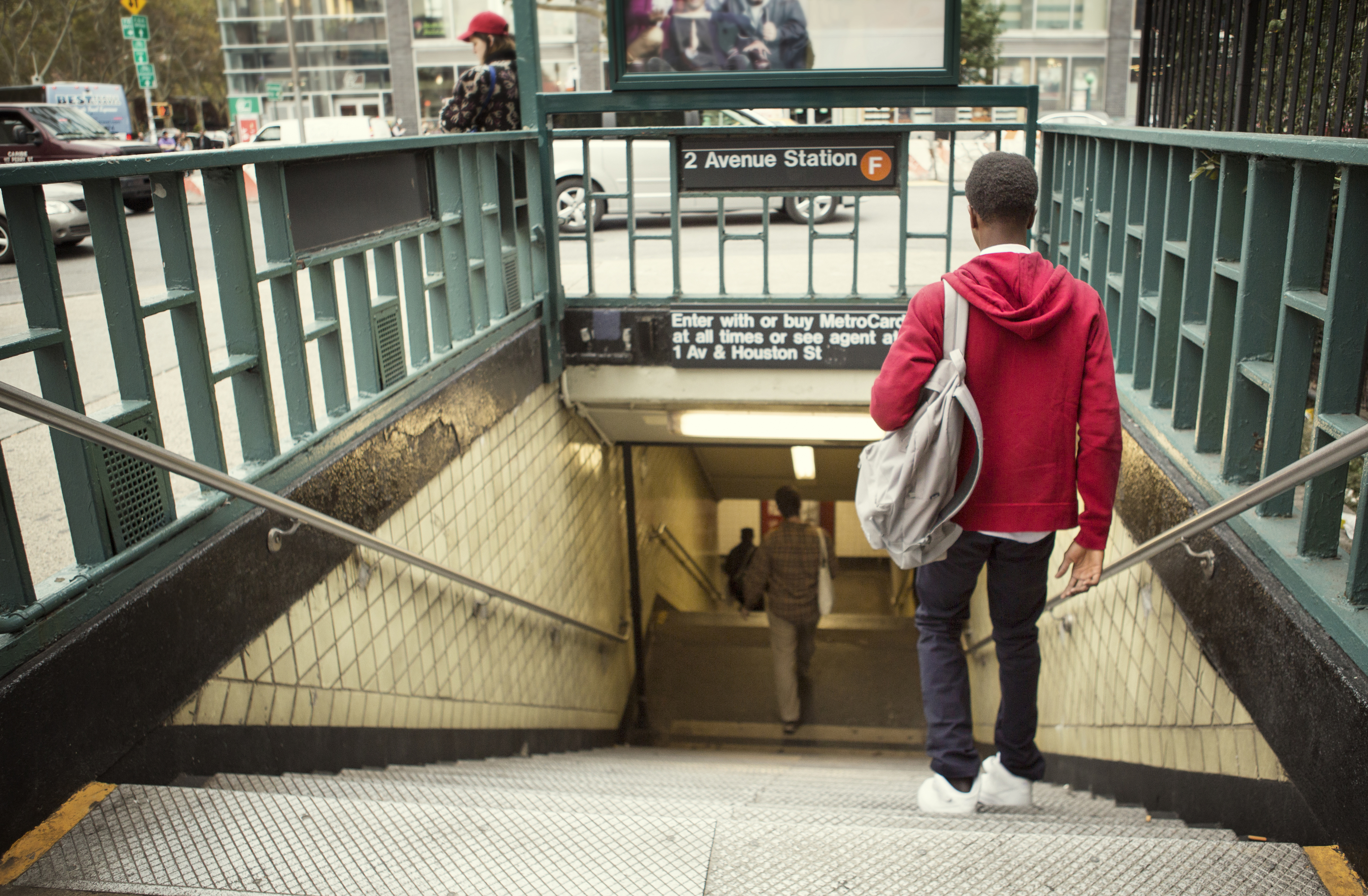 Person with a backpack descends subway stairs at 2 Avenue Station, sign for MetroCard purchase visible