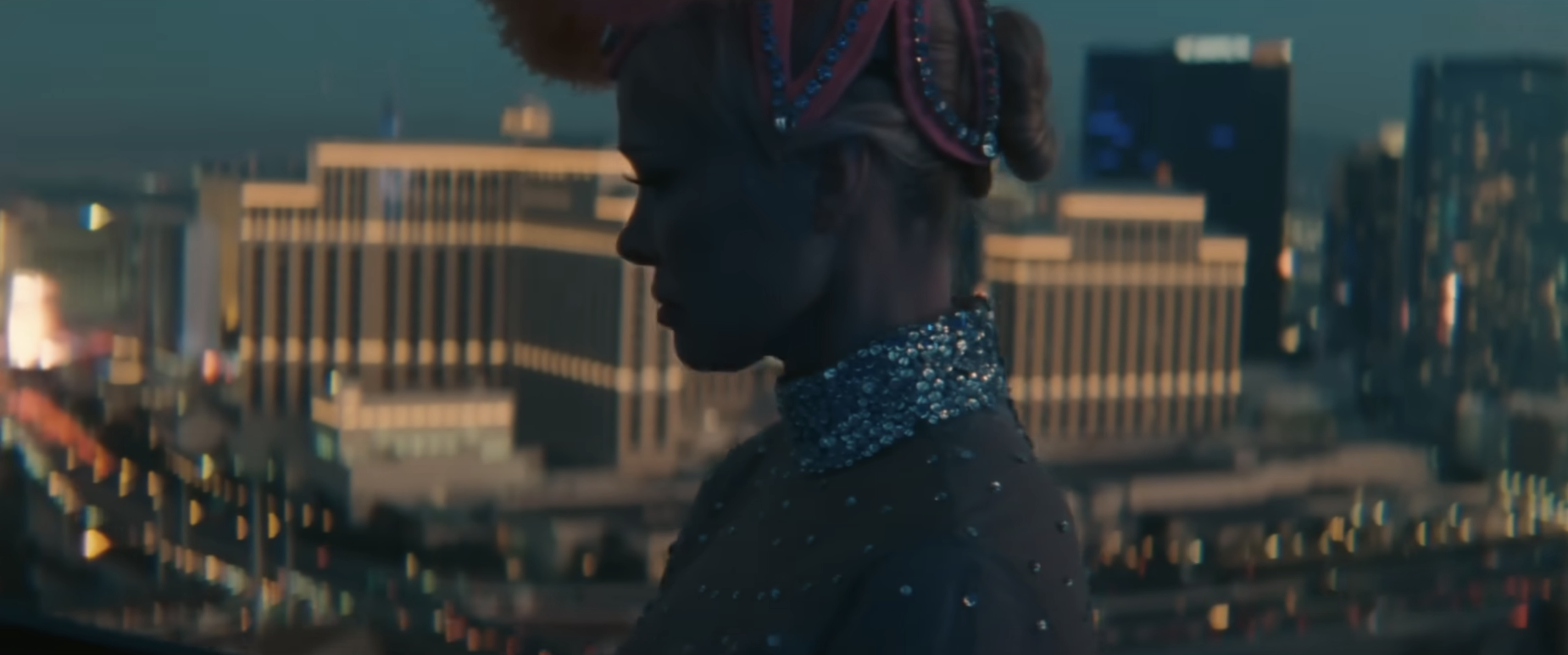 Pamela Anderson in profile wearing a beaded top and headband, with a city skyline in the background