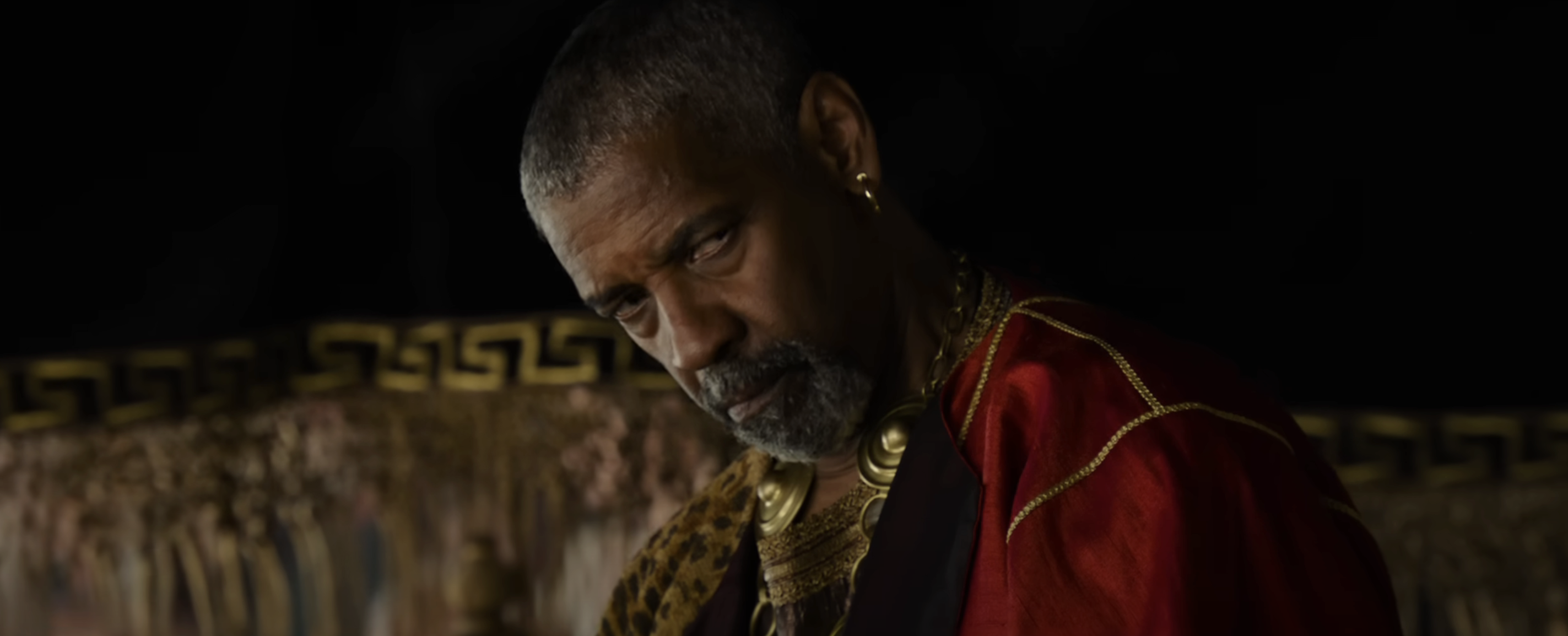 Denzel Washington  in ornate attire with gold accents gazes intensely. Background features intricate detailing, suggesting a dramatic or historical setting