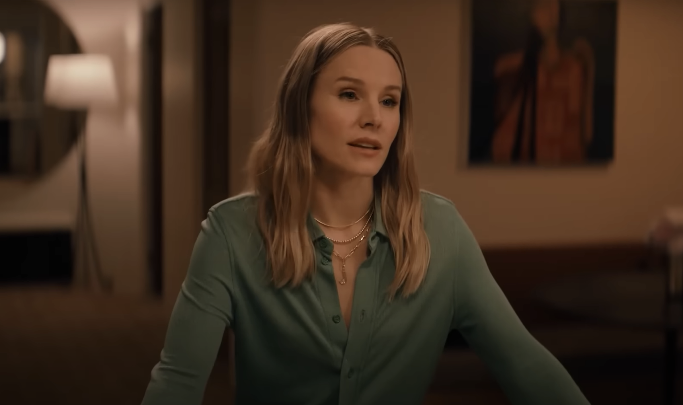 Kristen Bell in a casual setting wearing a buttoned shirt with layered necklaces, speaking or engaged in conversation