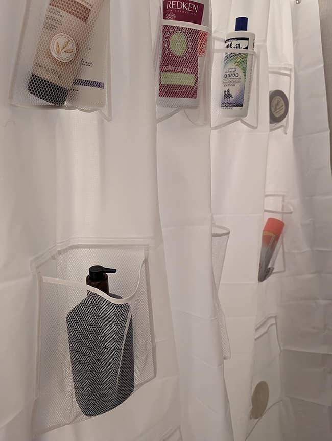 Shower curtain with pockets holding various personal care items, including lotions, shampoo, and a makeup brush set