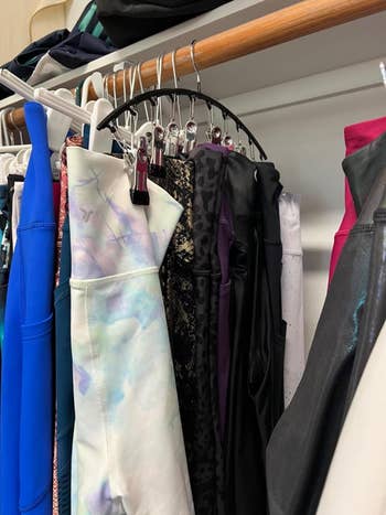 A variety of leggings in different patterns and textures are hung on hangers in a closet. They include floral, leopard print, shiny, and solid styles