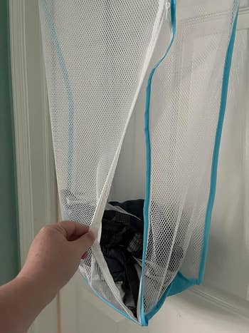 Close-up of a hand pulling open a mesh laundry hamper containing clothes