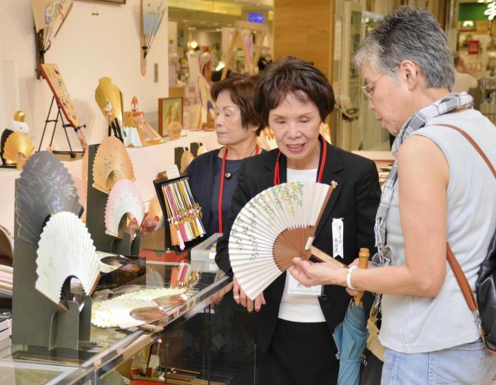 扇子を広げ、あおぎ心地を確かめる買い物客（右）＝１８日午前、松山市湊町５丁目