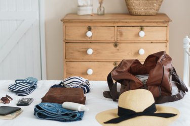 white bed with weekender bag, clothes, and hat