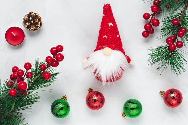 Albero di Natale con decorazioni di Capodanno e folletto su sfondo chiaro. Carta regalo celebrazione con rami di pino e bacche di agrifoglio rosso. Design piatto.