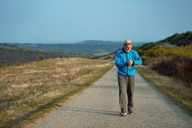 Foto gratuita atleta senior attivo che controlla la traccia del polso sull'orologio intelligente mentre cammina per strada in natura spazio di copia