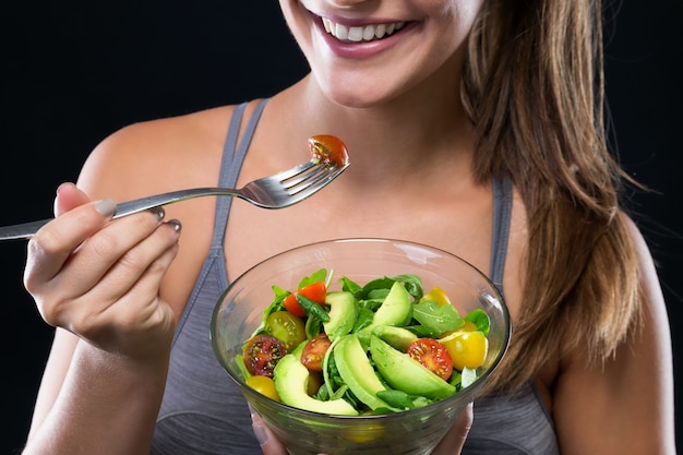 Foto gratuita bella giovane donna che mangia insalata sopra priorità bassa nera.