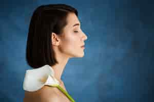 Foto gratuita chiuda sul ritratto di giovane donna tenera con il fiore bianco sopra la parete blu