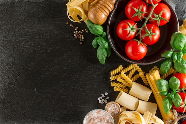 Foto gratuita composizione con varietà di pasta, pomodori e basilico su superficie scura